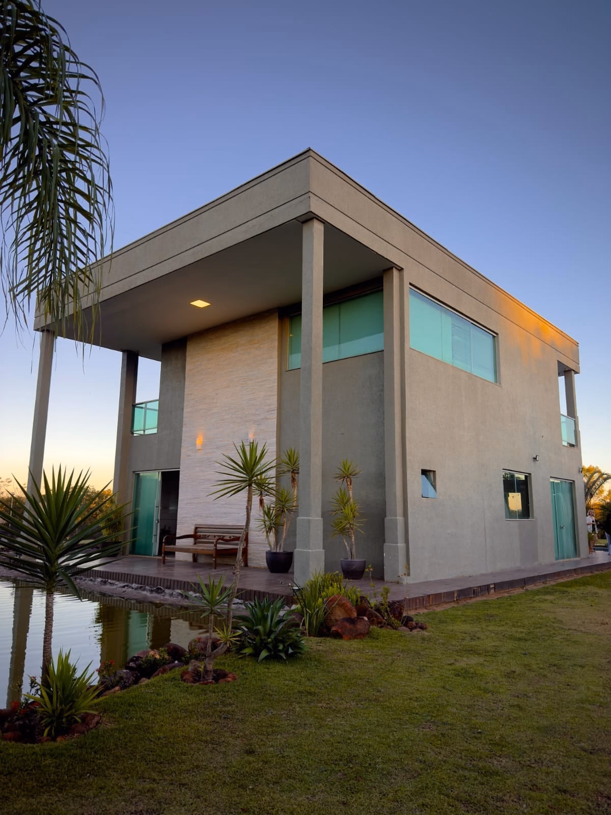 Fachada da casa ao anoitecer, luzes acesas e reflexo na água