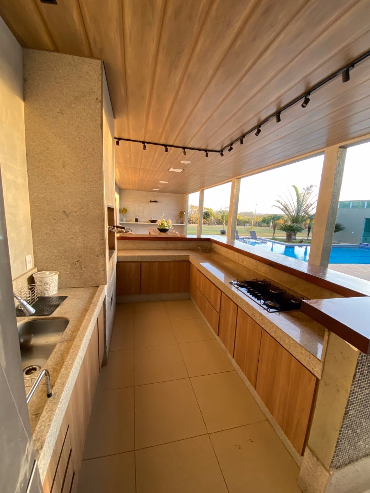 Bancada extensa da área gourmet com pia, piscina ao fundo