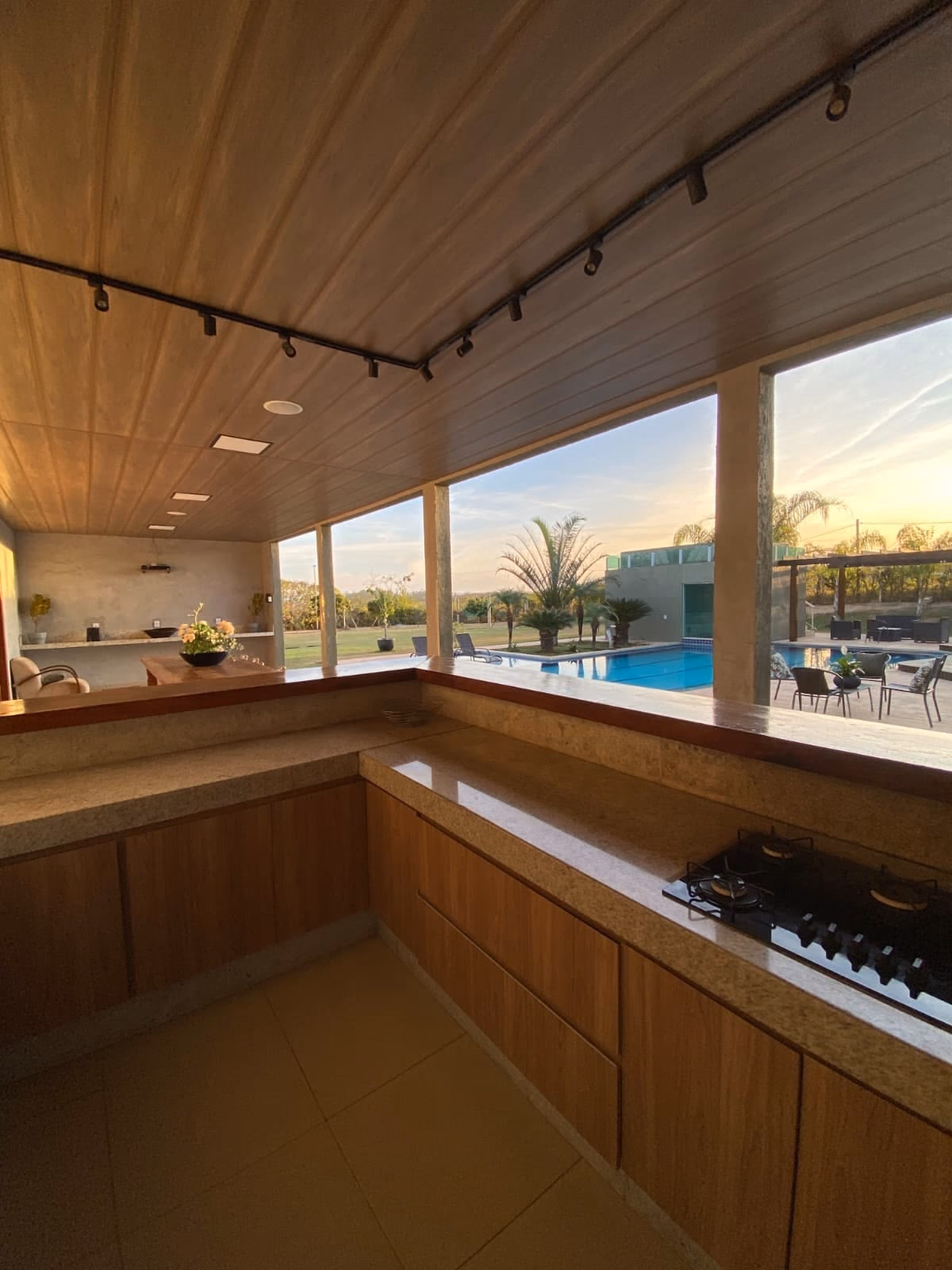 Cozinha de apoio da área gourmet com cooktop e vista da piscina ao entardecer