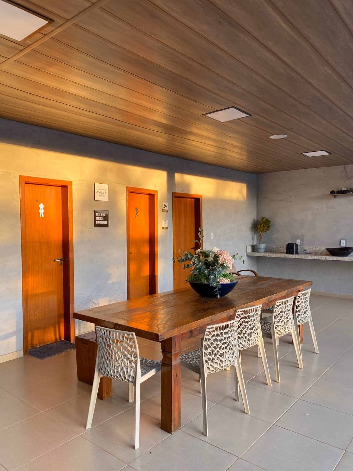 Área gourmet com mesa de madeira e corredor de acesso aos banheiros
