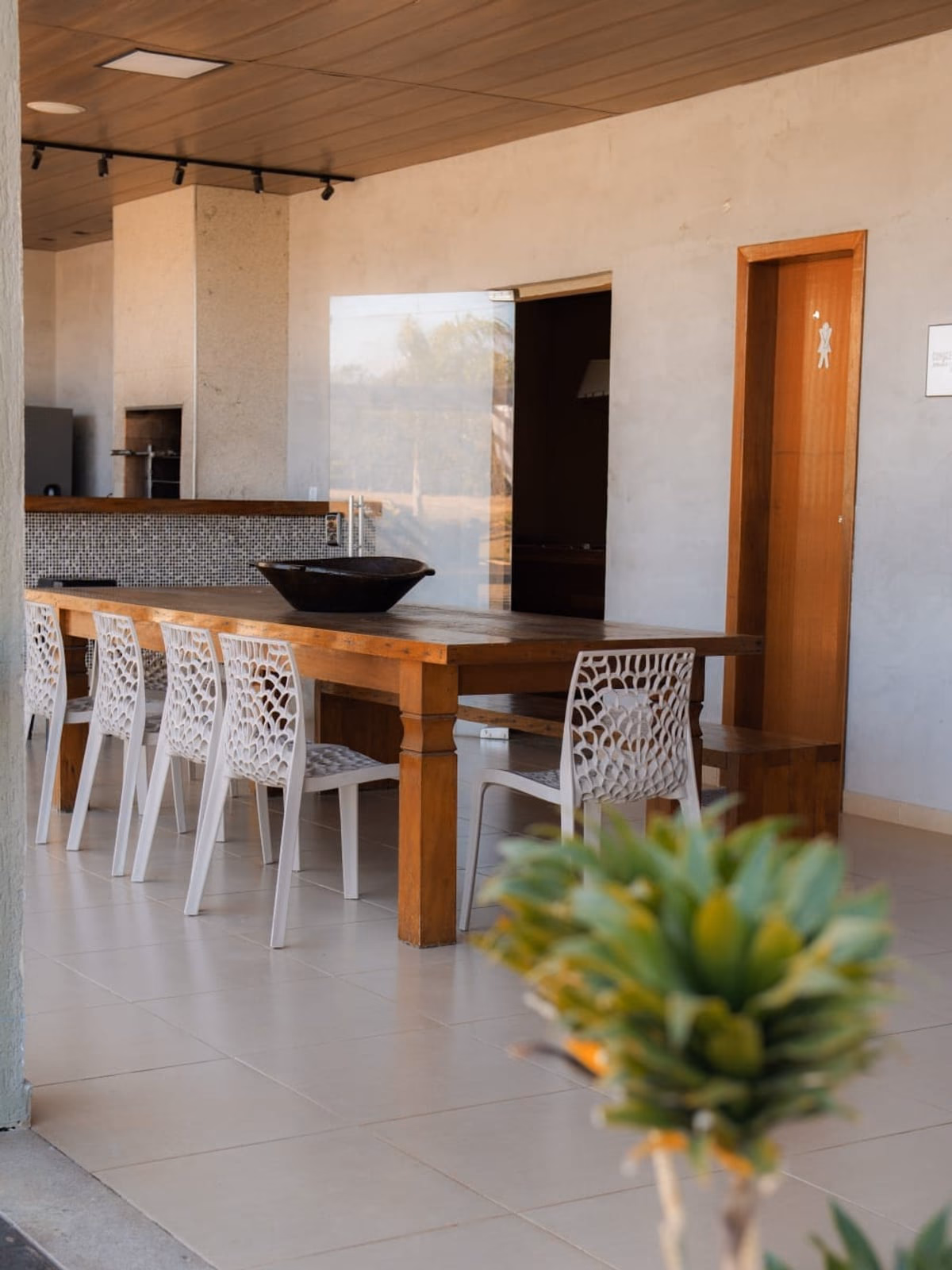 Área gourmet coberta com mesa longa e cadeiras brancas modernas