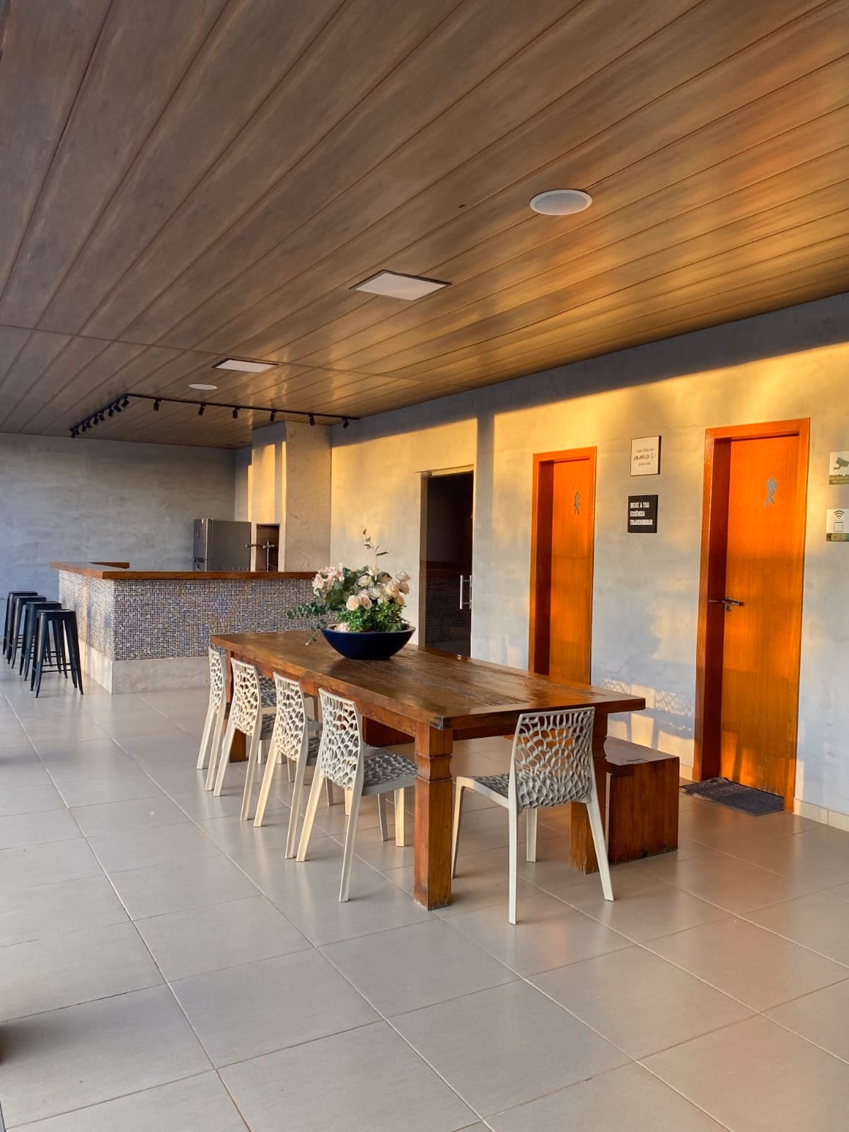 Mesa longa da área gourmet com flores e portas em laranja ao fundo
