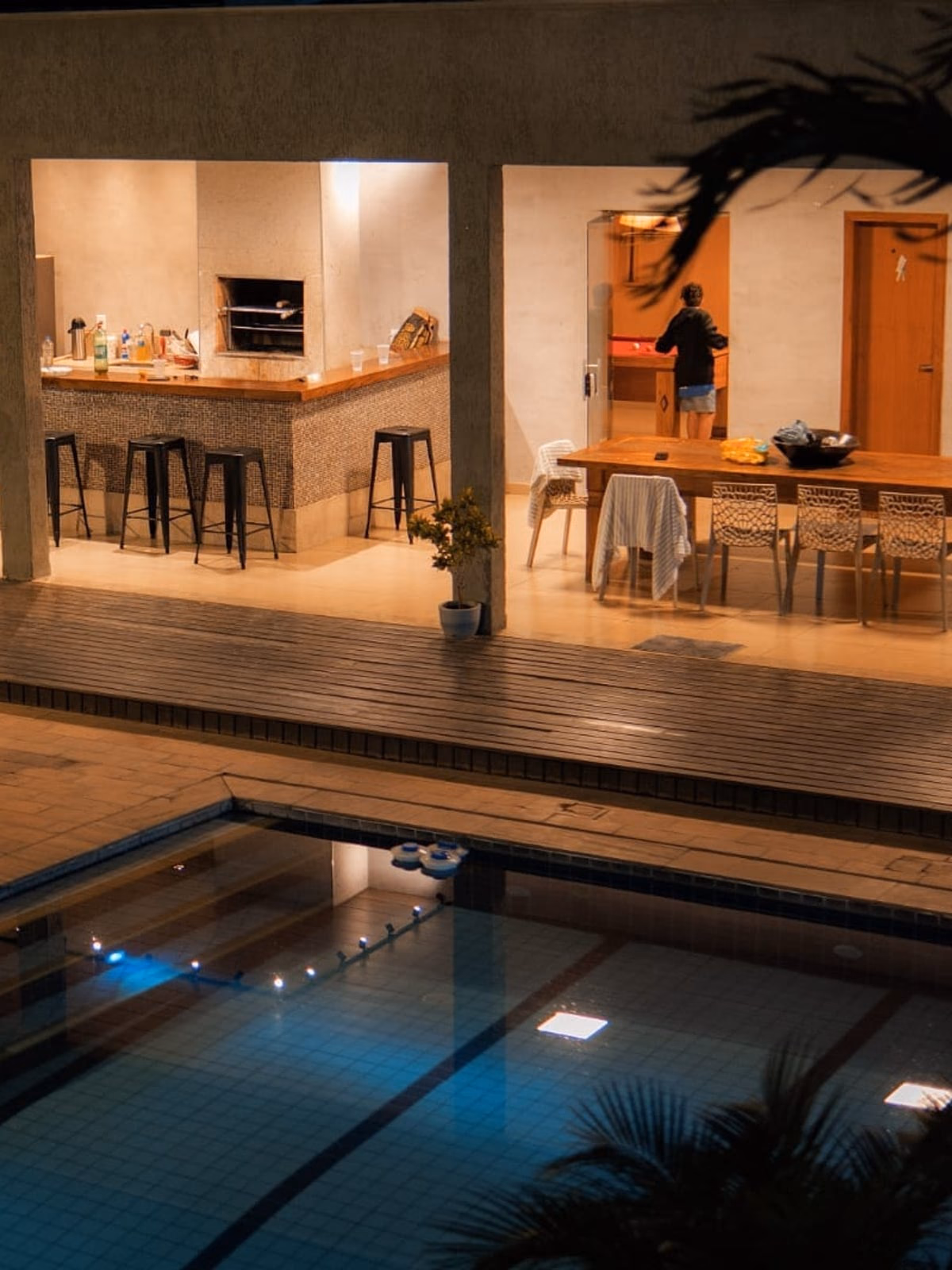 Área gourmet vista do mezanino à noite, piscina iluminada ao fundo