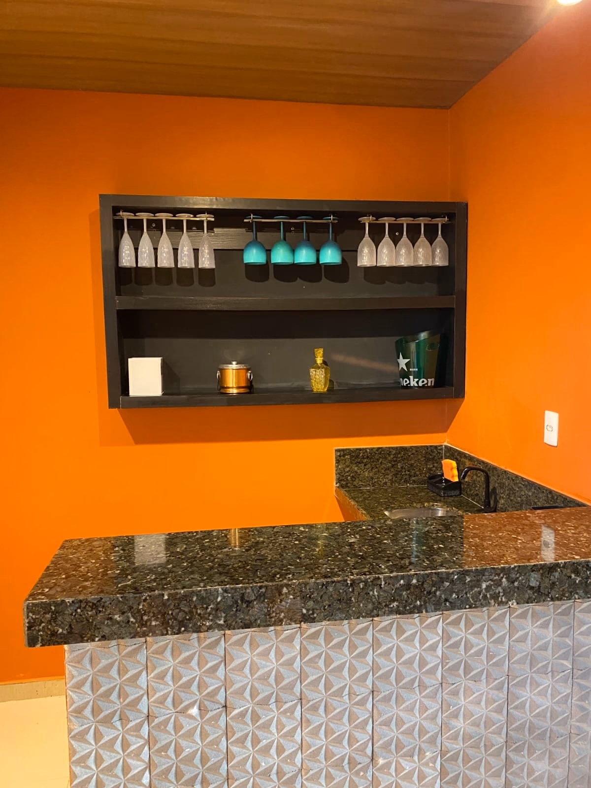 Bar da sala de jogos com taças penduradas e balcão de granito