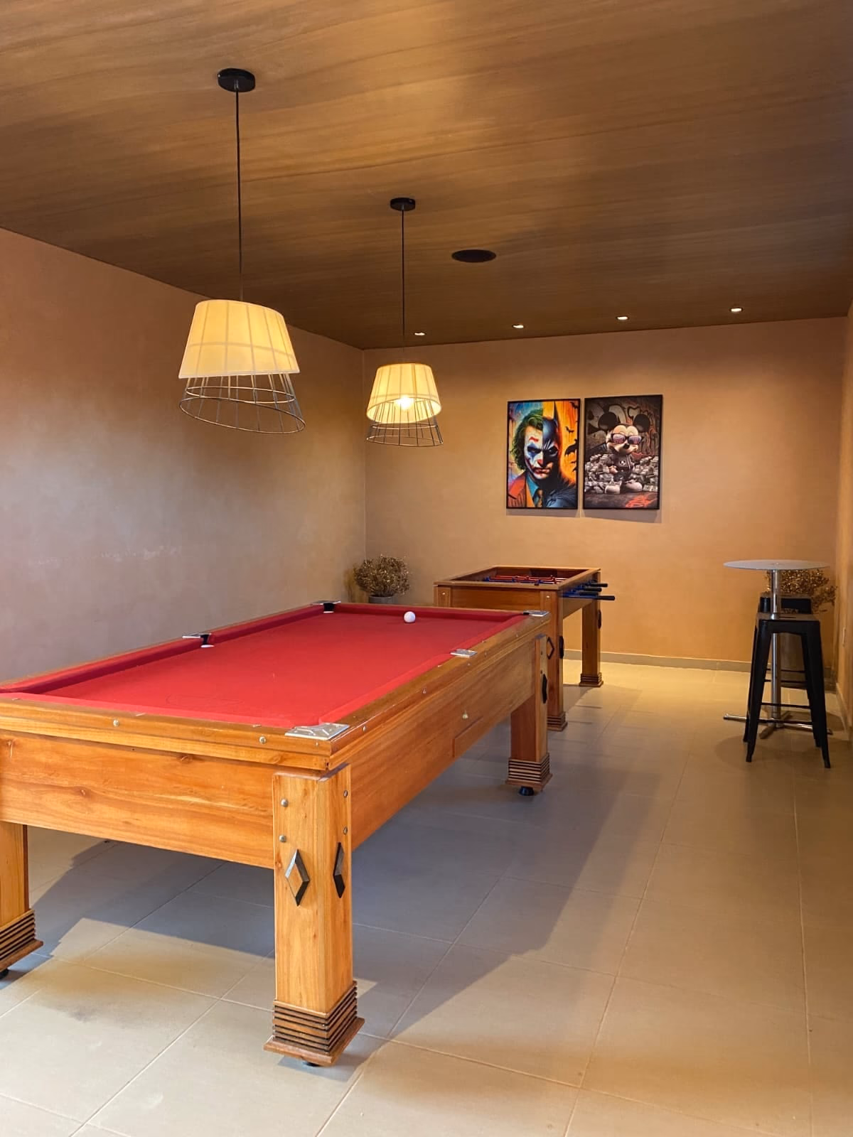 Sala de jogos com mesa de sinuca, totó ao fundo e quadros na parede