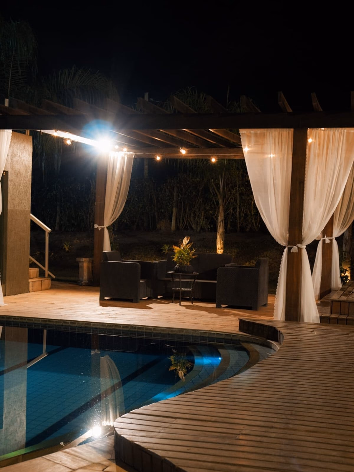 Piscina e pergolado iluminados à noite, deck em primeiro plano