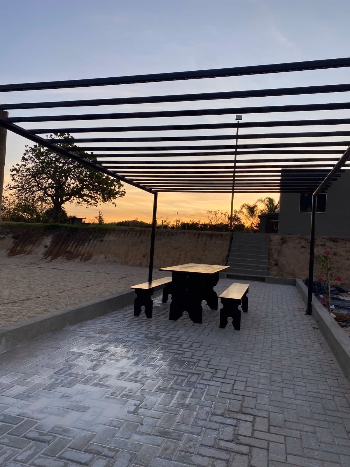 Quadra de areia com pergolado, mesa e bancos, entardecer