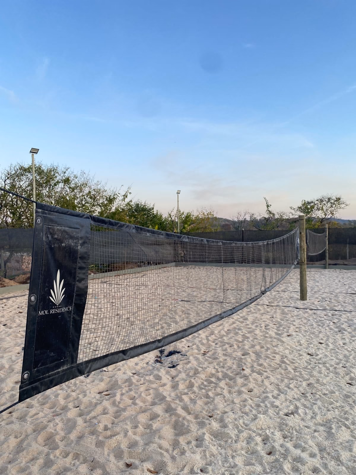 Rede de vôlei de areia com o logo da Mol Residence, entardecer