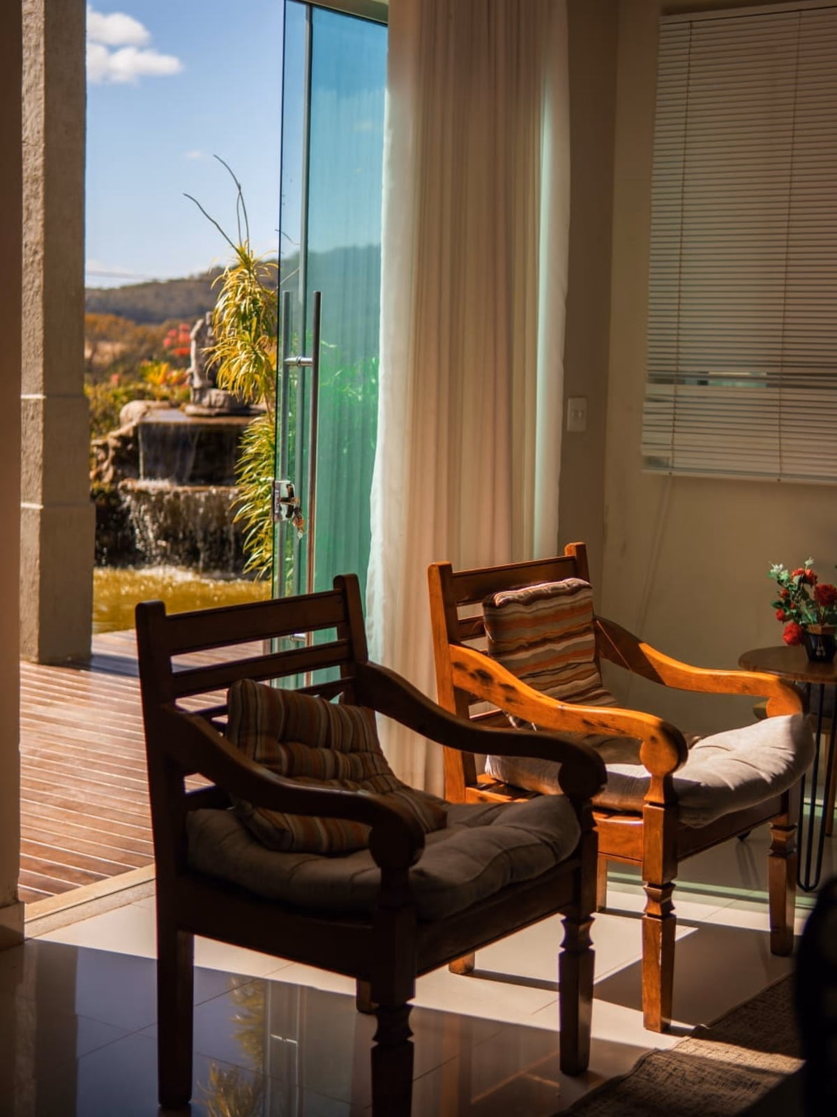 Sala integrada à varanda, com poltronas de madeira e vista para a fonte